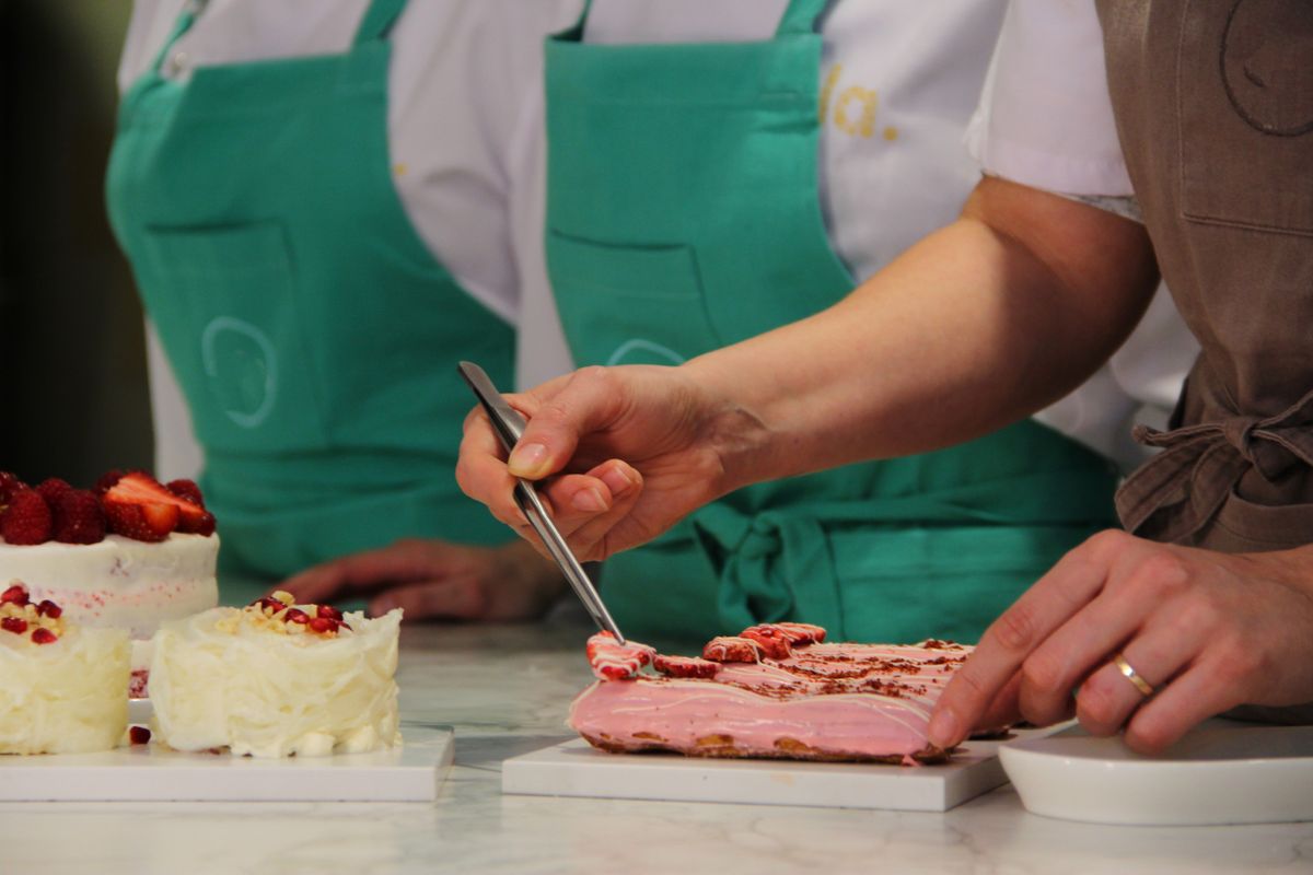 Close-up of pastry chefs in aprons meticulously decorating gourmet cakes with precision and artistry.