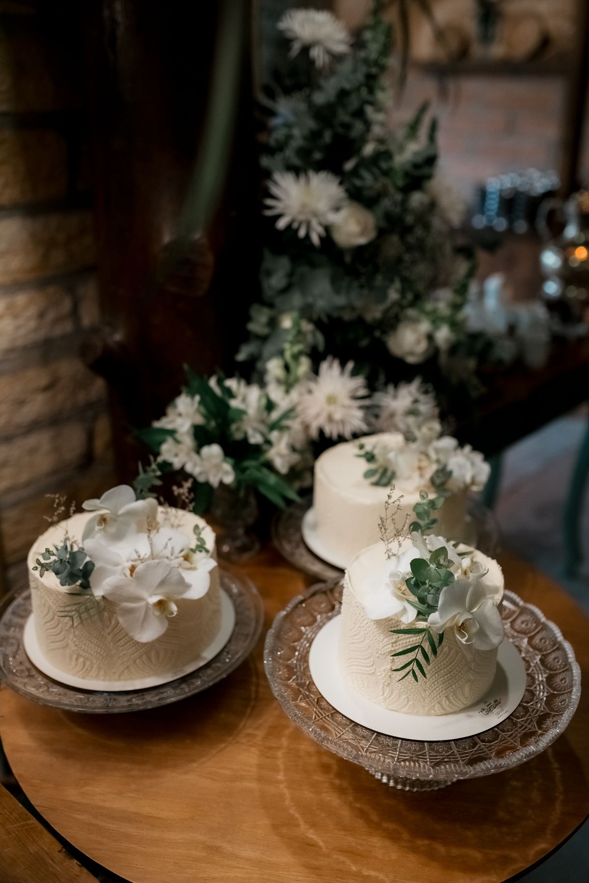 Three elegant floral wedding cakes with greenery are beautifully arranged indoors.